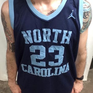 May include: Navy blue basketball jersey with light blue accents. The jersey features the words "NORTH CAROLINA" and the number "23" in light blue. A small Jumpman logo is visible on the chest.
