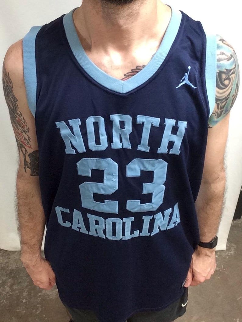 May include: Navy blue basketball jersey with light blue accents. The jersey features the words "NORTH CAROLINA" and the number "23" in light blue. A small Jumpman logo is visible on the chest.