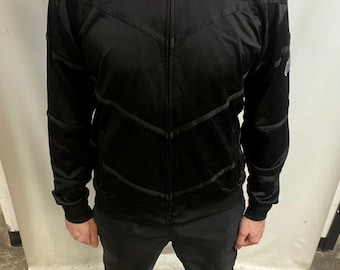 May include: Black track jacket with a full-length zip and a high collar. The jacket has a chevron design across the chest and upper arms. The matching black trousers complete the outfit.