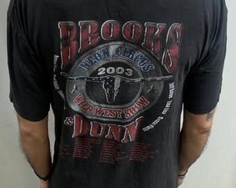 May include: Black t-shirt with a graphic for the Brooks & Dunn Neon Circus 2003 tour. The design includes the text "Neon Circus," "Wild West Show," and the names Brooks & Dunn. The graphic is in red, blue, and white.