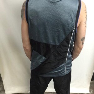 Puede incluir: Camiseta de baloncesto gris y negra con ribete azul alrededor del cuello y las sisas. La camiseta tiene un dise&ntilde;o diagonal negro en la parte delantera y una raya blanca en el lateral. La camiseta se combina con pantalones negros.