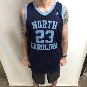 May include: A navy blue basketball jersey with light blue accents. The jersey features the words "NORTH CAROLINA" and the number "23" in light blue. A small Jumpman logo is visible on the upper right chest.
