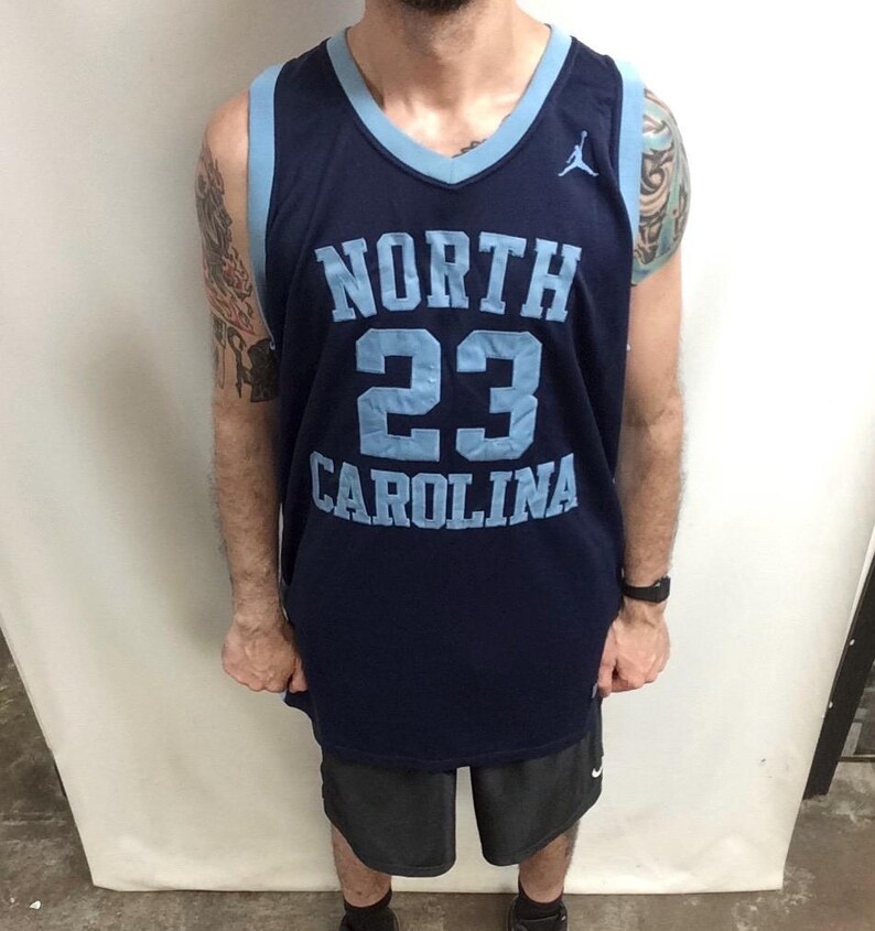 May include: A navy blue basketball jersey with light blue accents. The jersey features the words "NORTH CAROLINA" and the number "23" in light blue. A small Jumpman logo is visible on the upper right chest.