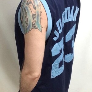 May include: Navy blue basketball jersey with light blue trim. The jersey features the name "JORDAN" and the number "23" in light blue lettering on the back. The jersey is sleeveless.
