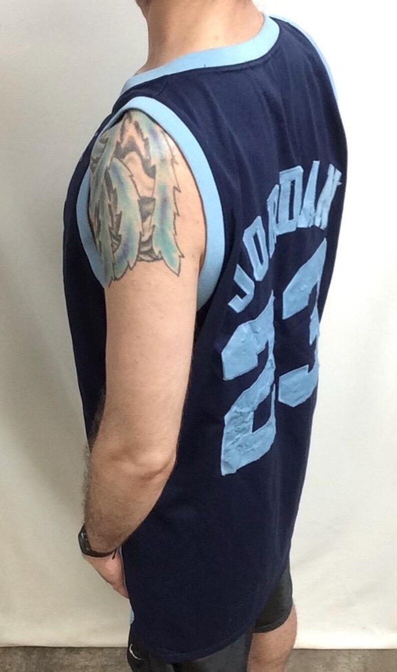 May include: Navy blue basketball jersey with light blue trim. The jersey features the name "JORDAN" and the number "23" in light blue lettering on the back. The jersey is sleeveless.