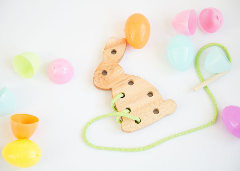 May include: A wooden bunny shaped lacing toy with holes for threading a green string.  The toy is surrounded by colorful plastic Easter eggs.