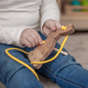 May include: A child is playing with a wooden toy animal. The toy is brown and has yellow buttons. The child is threading a yellow string through the holes in the toy.