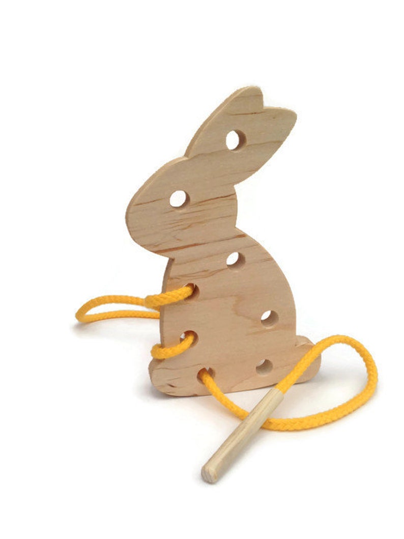 May include: Wooden bunny shaped lacing toy with yellow string and a wooden dowel. The bunny has holes for threading the string.