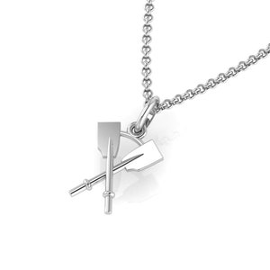 May include: A silver-colored pendant necklace featuring a crossed oars design. The pendant is a detailed, three-dimensional representation of two oars, with a chain attached for wearing. The necklace is displayed against a white background.