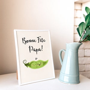 May include: A white picture frame with a white mat and a white background. The frame is standing on a white surface. The image in the frame is a cartoon of two peas in a pea pod. The peas are smiling and have eyes. The text on the image reads 'Bonne Fete Papa!'.
