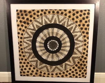 May include: Framed artwork with a circular design. The artwork features concentric circles in black, beige, and white, with a dotted pattern in the outer ring. The frame is dark brown.