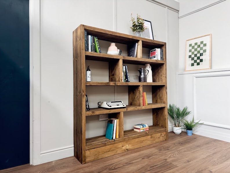 Puede incluir: Una gran estanter&iacute;a de madera r&uacute;stica con m&uacute;ltiples compartimentos. Los estantes est&aacute;n llenos de libros, objetos decorativos y una m&aacute;quina de escribir antigua. La madera tiene un acabado c&aacute;lido y natural, contra una pared blanca.