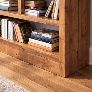 Puede incluir: Una estanter&iacute;a de madera llena de libros de varios tama&ntilde;os y colores. La estanter&iacute;a es de madera marr&oacute;n claro y tiene varios estantes. Los libros est&aacute;n apilados ordenadamente, creando un aspecto acogedor y organizado. La estanter&iacute;a est&aacute; colocada contra una pared.