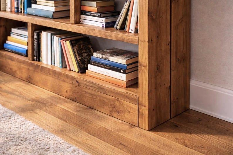 Puede incluir: Una estanter&iacute;a de madera llena de libros de varios tama&ntilde;os y colores. La estanter&iacute;a es de madera marr&oacute;n claro y tiene varios estantes. Los libros est&aacute;n apilados ordenadamente, creando un aspecto acogedor y organizado. La estanter&iacute;a est&aacute; colocada contra una pared.