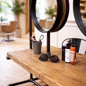 K&ouml;nnte beinhalten: Holztisch mit schwarzen Metallbeinen und einer runden Sonnenbrille. Zwei kreisf&ouml;rmige Spiegel mit schwarzem und Holzbesatz sind &uuml;ber dem Tisch montiert. Ein kleiner Metallbeh&auml;lter enth&auml;lt eine Schere.