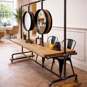 K&ouml;nnte beinhalten: Ein rustikaler Salon-Arbeitsplatz mit einer Holzplatte und einem schwarzen Metallrahmen. Zwei kreisf&ouml;rmige Spiegel mit Holz- und schwarzem Besatz h&auml;ngen &uuml;ber dem Tisch. Der Arbeitsplatz umfasst einen Schnurrbart-Dekoration, Flaschen und Gl&auml;ser. Der Arbeitsplatz ist auf R&auml;dern.
