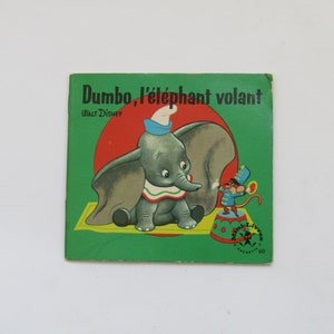 May include: Vintage children's book cover featuring Dumbo the elephant. The cover is green with the title "Dumbo, l'&eacute;l&eacute;phant volant" and Walt Disney's name. Dumbo is depicted with a blue hat and a mouse in a circus outfit.