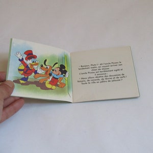 May include: A vintage children's book featuring Mickey Mouse, Pluto, and Donald Duck. The book's cover is green and features a cartoon illustration of the three characters. The text on the open page reads: "Bonjour, Pluto! -  de l'oncle Picsou le lendemain matin, en voyant arriver son chien de chasse. L'oncle Picsou est terriblement agit&eacute; et il annonce: Nous allons abattre des douzaines de faisans, de canards, de li&egrave;vres et de cerfs! Toute la ville en p&acirc;lira de jalousie!"