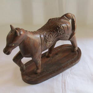 May include: A dark brown wooden horse sculpture with intricate carvings on its back and a detailed face. The horse is standing on a wooden base.