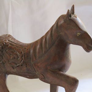 May include: A hand-carved wooden horse sculpture with intricate details. The horse is brown and has a detailed mane and tail. The horse is standing on all four legs and has a slightly tilted head.
