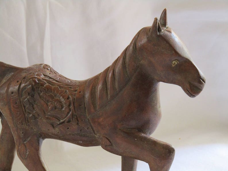 May include: A hand-carved wooden horse sculpture with intricate details. The horse is brown and has a detailed mane and tail. The horse is standing on all four legs and has a slightly tilted head.