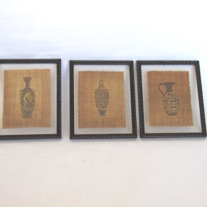 May include: Three framed artworks displaying ancient vase illustrations on textured, tan paper. Each black framed piece presents a different vase design in dark grey, offering a glimpse into classical art and decor.