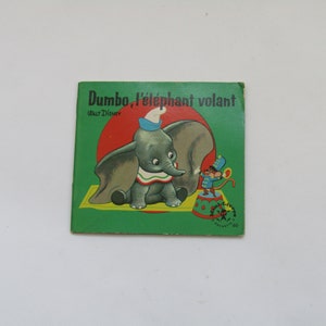 May include: Vintage children's book cover featuring Dumbo the elephant. The cover has a green background with the title "Dumbo, l'&eacute;l&eacute;phant volant" and a cartoon illustration of Dumbo and a mouse. The book is a Walt Disney production.