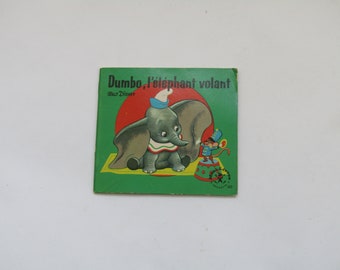 May include: Vintage children's book cover featuring Dumbo the elephant. The cover has a green background with the title "Dumbo, l'éléphant volant" and a cartoon illustration of Dumbo and a mouse. The book is a Walt Disney production.