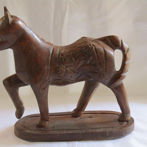 May include: A dark brown wooden horse figurine with intricate carvings on its body and a base. The horse is standing on its four legs with its head held high.
