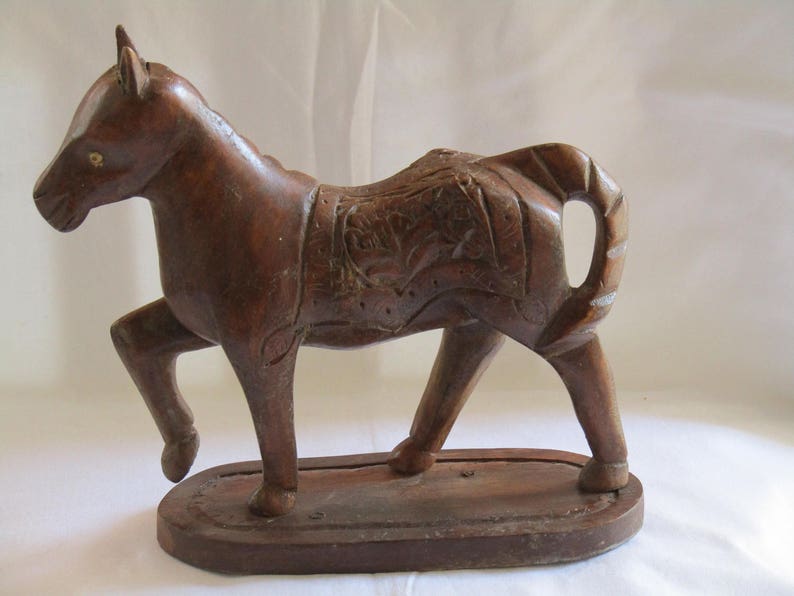 May include: A dark brown wooden horse figurine with intricate carvings on its body and a base. The horse is standing on its four legs with its head held high.