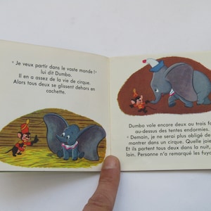May include: Open book with illustrations from a children's story. The images depict Dumbo the elephant and a mouse in a circus setting. Text in French accompanies the illustrations.
