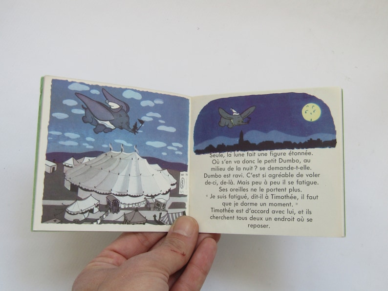 May include: A vintage children's book featuring illustrations of Dumbo the elephant. The open pages show Dumbo flying at night, with a circus tent in the background. The book has a green border.