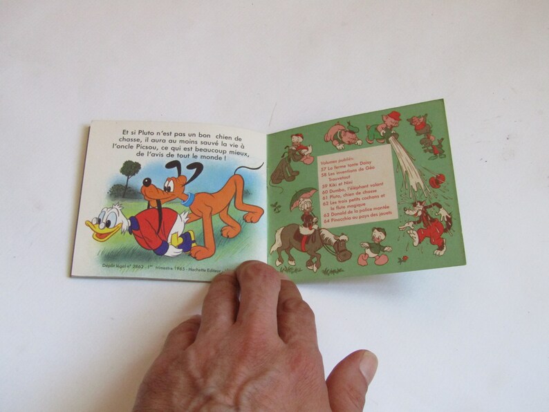 May include: An open book with a cartoon illustration of Pluto and Donald Duck. The book is titled "Donald Duck" and features a green cover with a white border. The text on the page reads "Et si Pluto n'est pas un bon chien de chasse, il aura au moins sauv&eacute; la vie &agrave; P'oncle Picsou, ce qui est beaucoup mieux, de l'avis de tout le monde!"