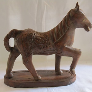 May include: A wooden horse sculpture with intricate carvings on its body. The horse is standing on a wooden base.