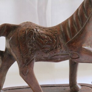 May include: A carved wooden horse figurine with intricate details. The horse is brown and has a saddle with floral designs. The figurine is standing on a wooden base.