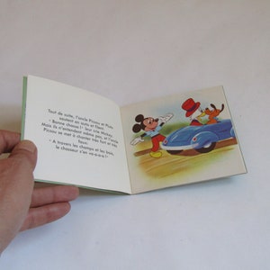 May include: A vintage children's book featuring Mickey Mouse and Donald Duck. The book is open to a page with a colorful illustration of Mickey Mouse waving goodbye to Donald Duck and Pluto as they drive away in a blue car. The text on the page reads: "Tout de suite, l'onde Picsou et Pus soutent en auto et filent Bonne chasse!" leur crie Mickey Mais ils n'entendent m&ecirc;me pas, et l'on Picsou se met &agrave; chanter tr&egrave;s fort et fous A travers les champs et les bois, le chasseur s'en voe"