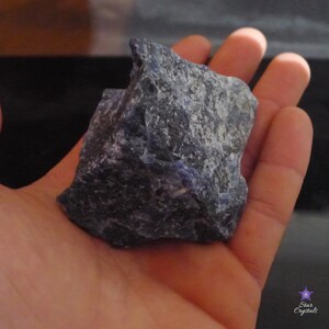 May include: A large, rough, dark blue and gray stone with a slightly purple hue. The stone is being held in a person's hand.