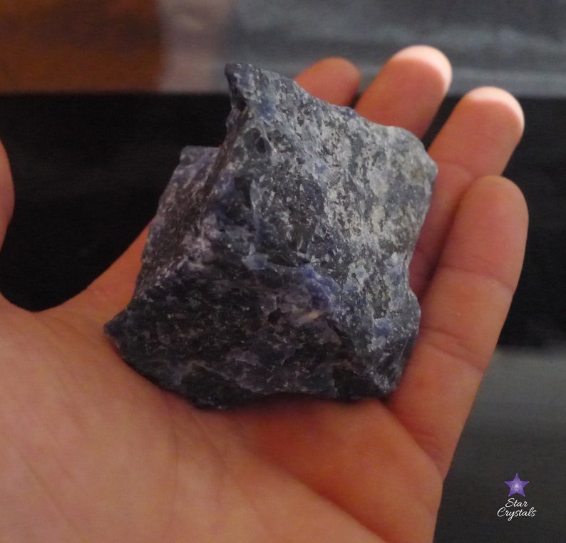 May include: A large, rough, dark blue and gray stone with a slightly purple hue. The stone is being held in a person's hand.