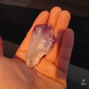 May include: A large, clear amethyst crystal with purple and white hues. The crystal is pointed at one end and has a rough, natural texture.