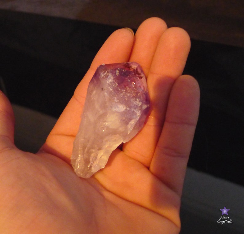 May include: A large, clear amethyst crystal with purple and white hues. The crystal is pointed at one end and has a rough, natural texture.