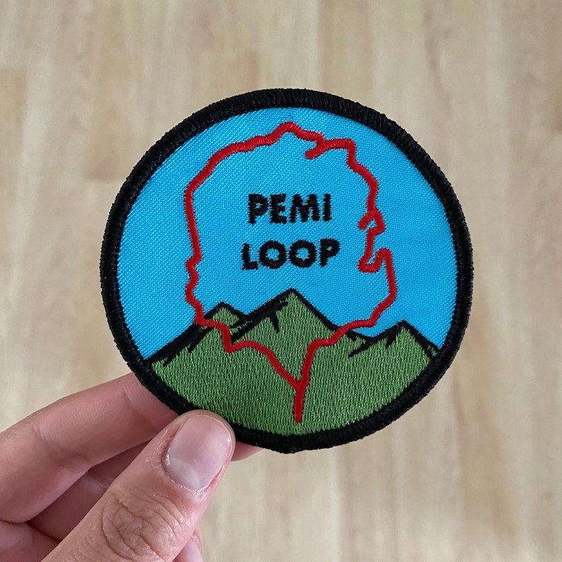 Pode incluir: Um remendo bordado azul e verde com um contorno vermelho da trilha Pemi Loop. O texto "PEMI LOOP" &eacute; bordado em preto.