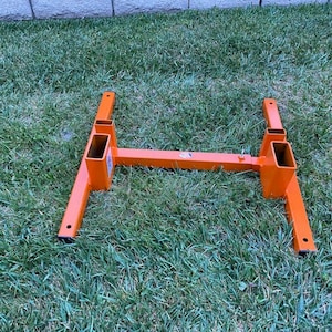 May include: Orange metal stand with four legs and two rectangular openings. The stand is on a green grassy surface.