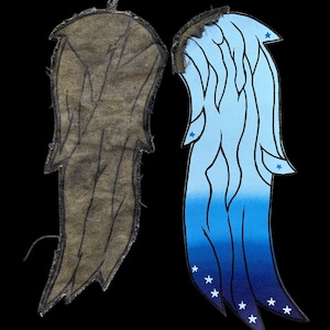 Op de afbeelding: Twee vleugelvormige patches met zwart gestikte randen. De ene patch toont een donkerbruine, getextureerde achterkant met zichtbare stiklijnen. De andere patch heeft een blauw kleurverloop van lichtblauw naar donkerblauw met witte sterren.