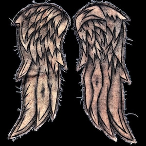 May include: A pair of embroidered fabric patches shaped like angel wings. The wings feature a tan and brown colour palette with detailed black stitching to define the individual feathers. The edges of the patches have a frayed, textured appearance.