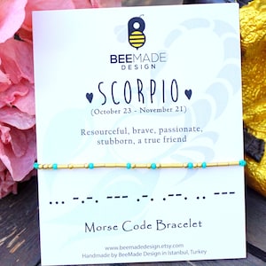 May include: A gold and turquoise beaded bracelet with a card that says "BeeMade Design" and "Scorpio (October 23 - November 21)". The card also says "Resourceful, brave, passionate, stubborn, a true friend" and "Morse Code Bracelet".