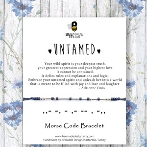 Pode incluir: Um bracelete de contas azuis e prateadas com um cartão que diz "UNTAMED." O cartão apresenta uma citação sobre abraçar o seu espírito selvagem e um bracelete de código Morse. O cartão também inclui o endereço do site e informações sobre o bracelete feito à mão.