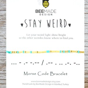 Puede incluir: Un brazalete de cuentas turquesa y dorado con el mensaje "STAY WEIRD" en código Morse. El brazalete está hecho a mano y viene con una tarjeta que dice "Deja que tu luz extraña brille para que los otros weirdos sepan dónde encontrarte."
