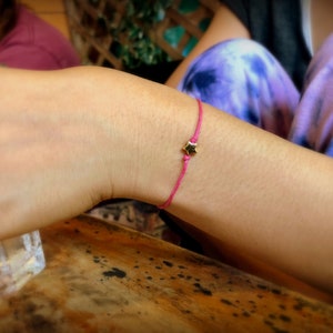 May include: A pink string bracelet with a gold star charm.