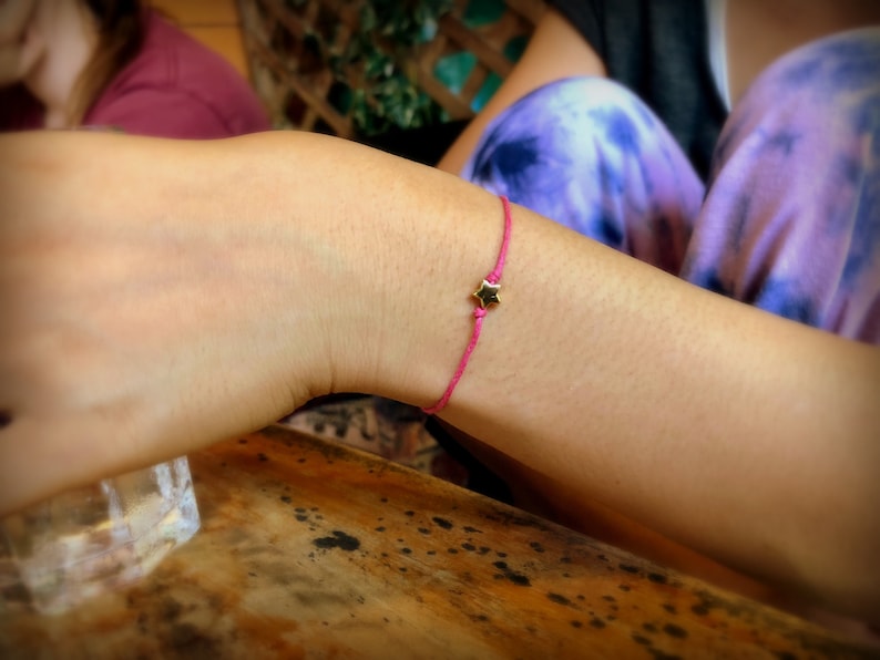 May include: A pink string bracelet with a gold star charm.