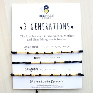 May include: A white card with the text "3 GENERATIONS" and three Morse code bracelets. The bracelets are black and gold, with the words "grandma", "mom", and "daughter" below each bracelet. The card also has the BeeMade Design logo.